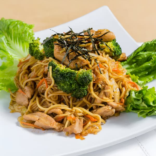 Chicken yakisoba noodles with broccoli, carrots, and seaweed on a white rectangular plate.