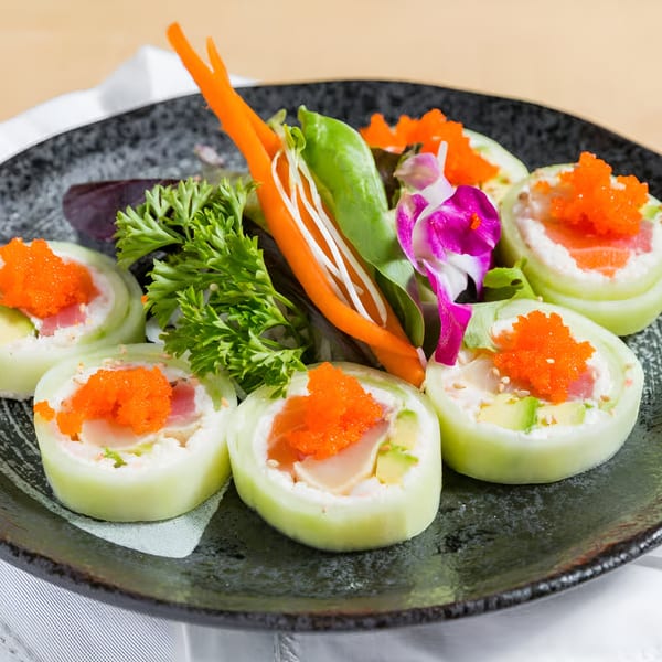 Kin Sushi's cucumber-wrapped sushi rolls with fish, avocado, and orange roe, garnished with greens and a flower.