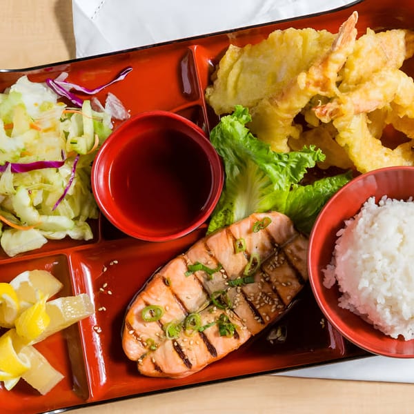 Kin Sushi bento box with grilled salmon, tempura, rice, salad, and lemon slices.