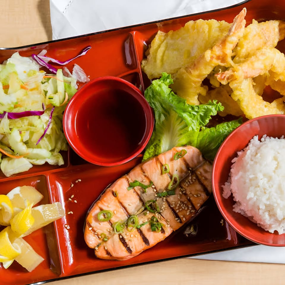 Kin Sushi bento box with grilled salmon, tempura, rice, salad, and lemon slices.