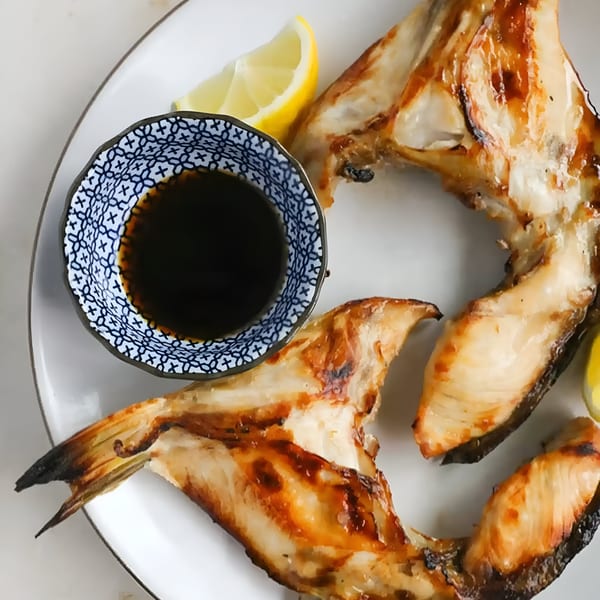 Grilled fish collars with lemon wedges and a small bowl of soy sauce on a white plate.