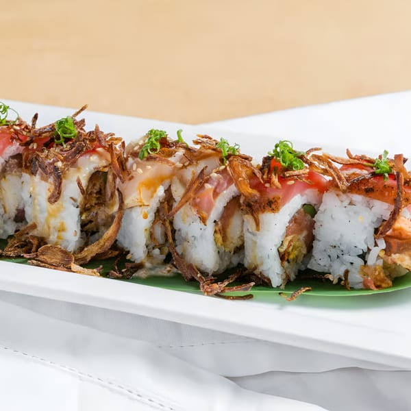 Kin Sushi's sushi roll with fried onions, green onions, and sesame seeds on a white plate.