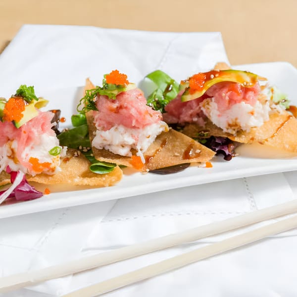 Three Kin Sushi tuna and crab tostadas with avocado, roe, and greens on a white plate.
